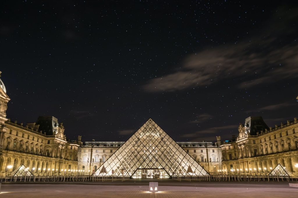Texto alternativo para una imagen del Louvre de noche, el emblemático museo de arte de París (Francia), iluminado por la noche.